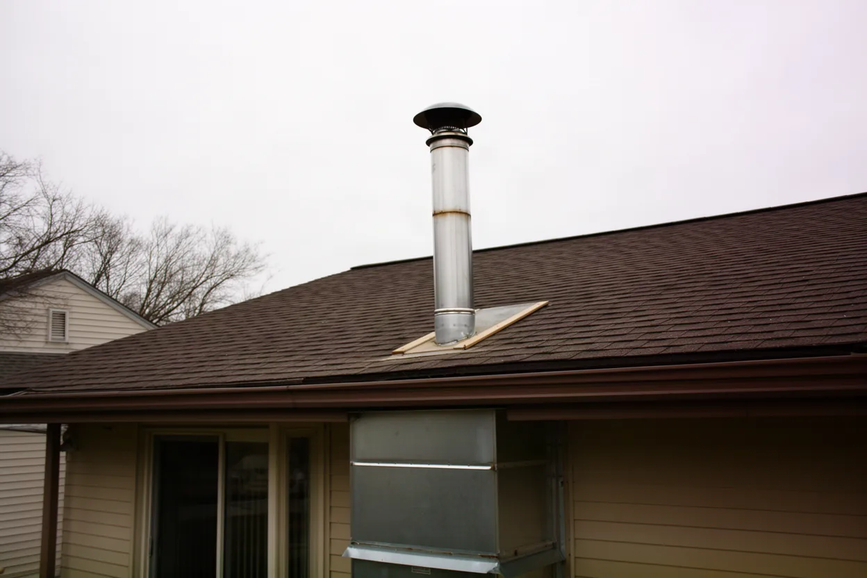 metal stove pipe chimney with a round cap on the roofline of a suburban home