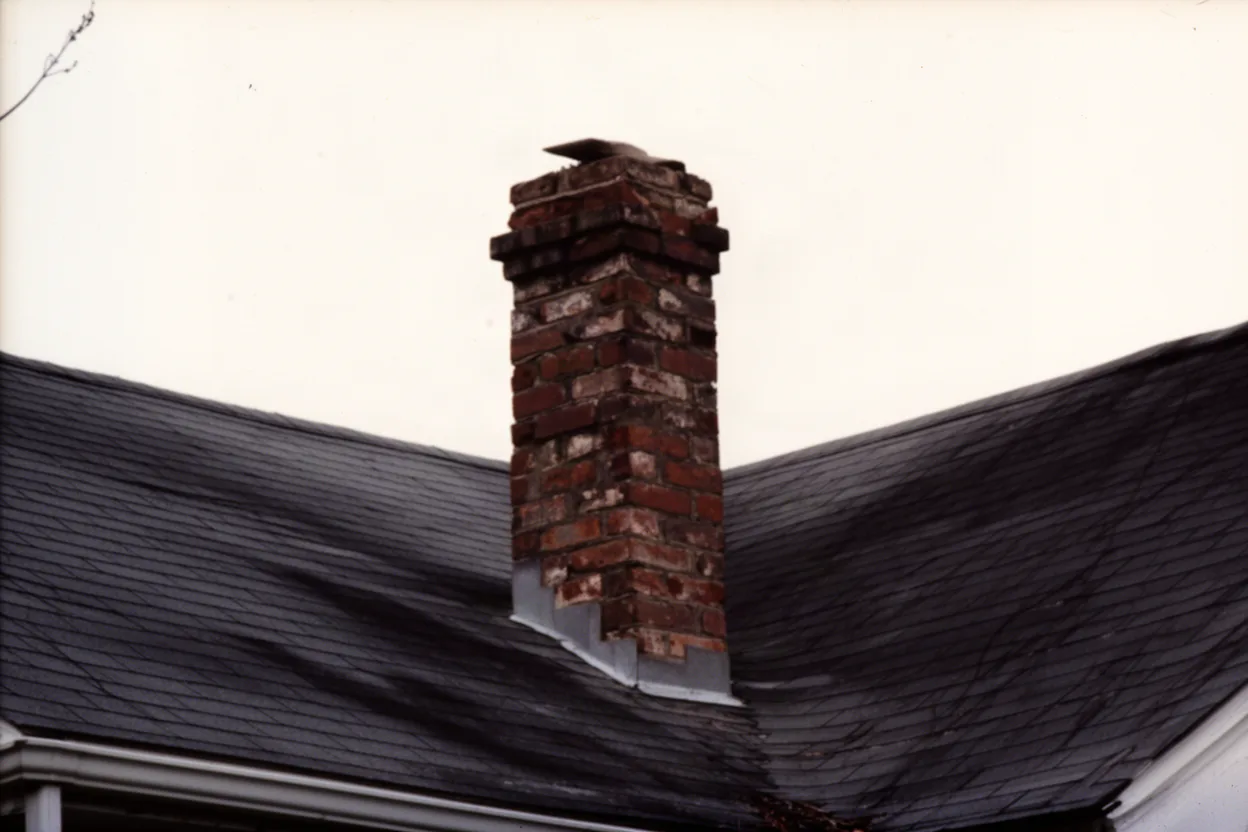 an old unreinforced brick chimney on an older house roofline, muted colors